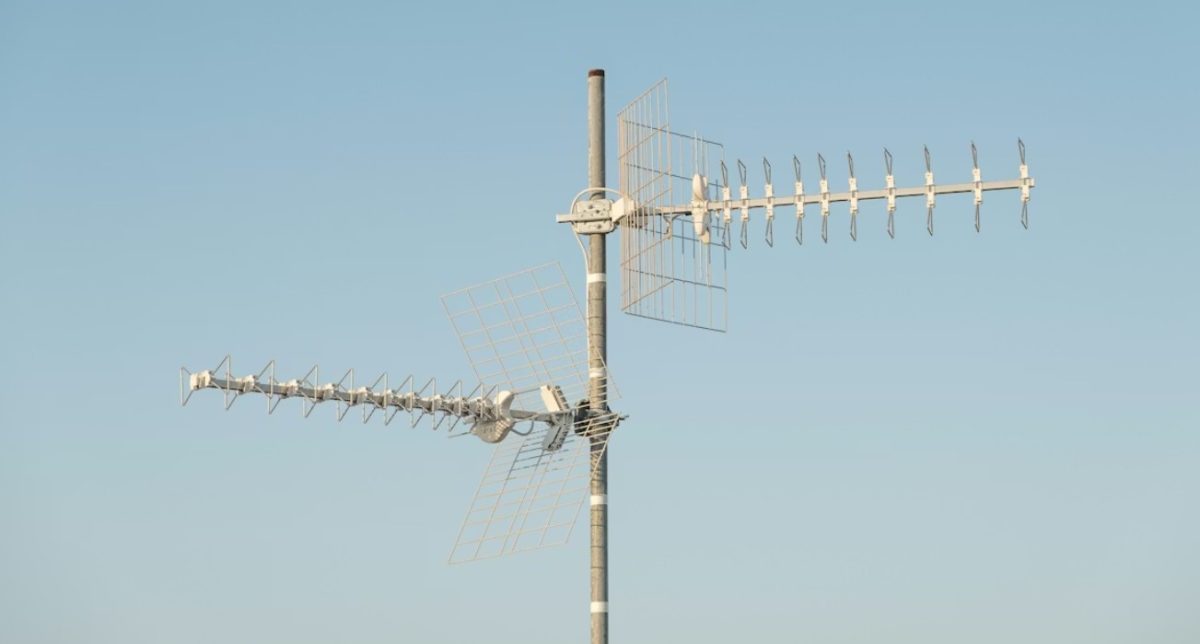 An image of a white antenna with two arms in a blue sky.