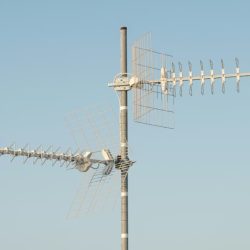 An image of a white antenna with two arms in a blue sky.